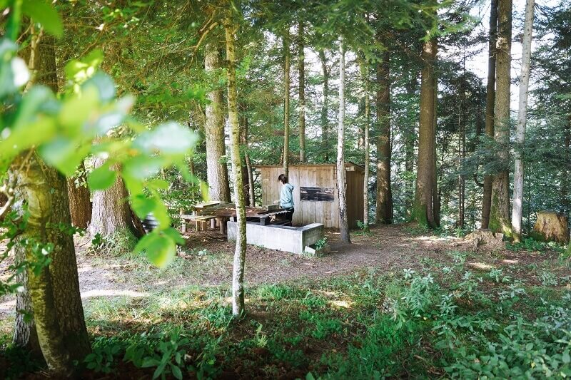 Campen in der Schweiz: Zeltplatz im Wald mit Sitzgelegenheit und kleiner Kochhütte