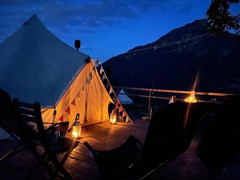 Zelten in der Schweiz: Glamping Zelt mit Wimpel und Beleuchtung am Abend und Bergblick