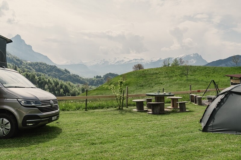 Campen in der Schweiz: Bus mit Hubdachzelt und Trekkingzelt auf Stellplatz mit Sitzgelegenheiten