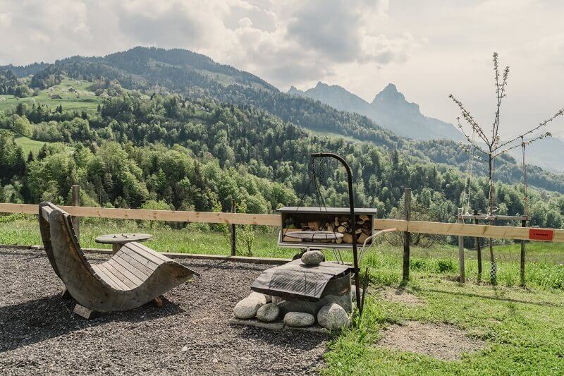 Glamping und Camping in der Schweiz: Feuerstelle und Relaxstuhl und Berge neben Stellplatz